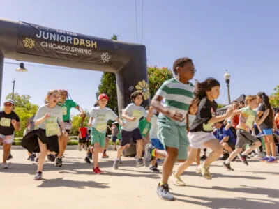 Children running under a Junior Dash Chicago Spring inflatable archway at the start line.