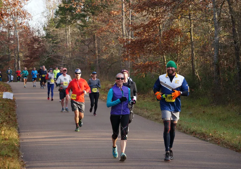 Runners on a paved path through a forest during a race.