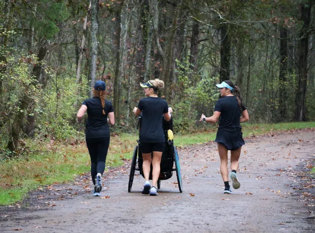 Three people running on a forest path, one in a wheelchair.