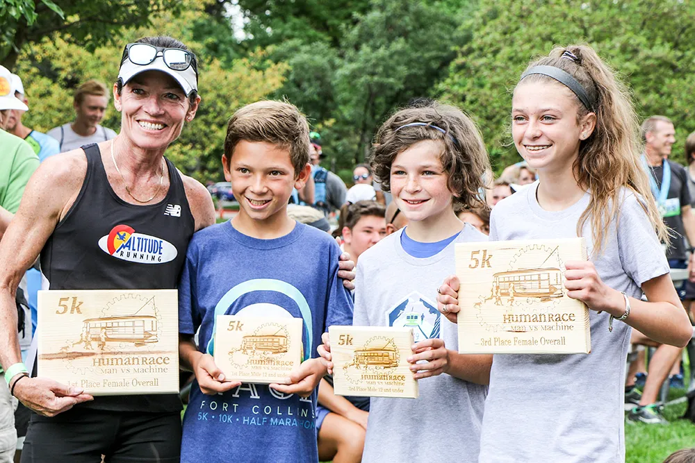 A group of runners, including children and an adult woman, smiling and holding awards after a race.