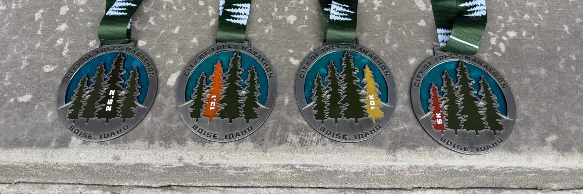 Four City of Trees Marathon medals for 26.2, 13.1, 10K, and 5K races, displayed on a concrete surface.