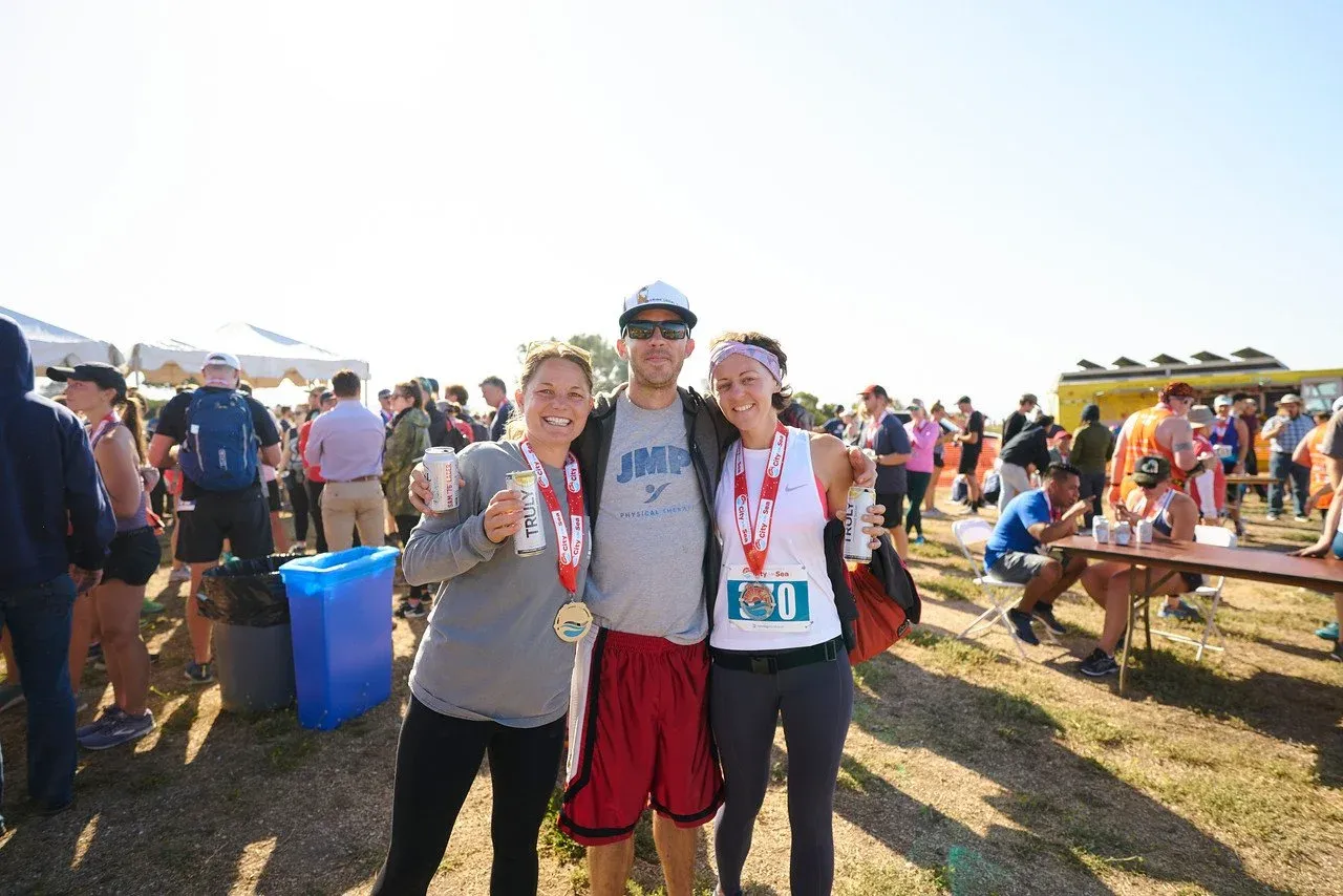 Three smiling runners, two women and one man, pose for a photo after a race, wearing medals and holding cans of Truly.