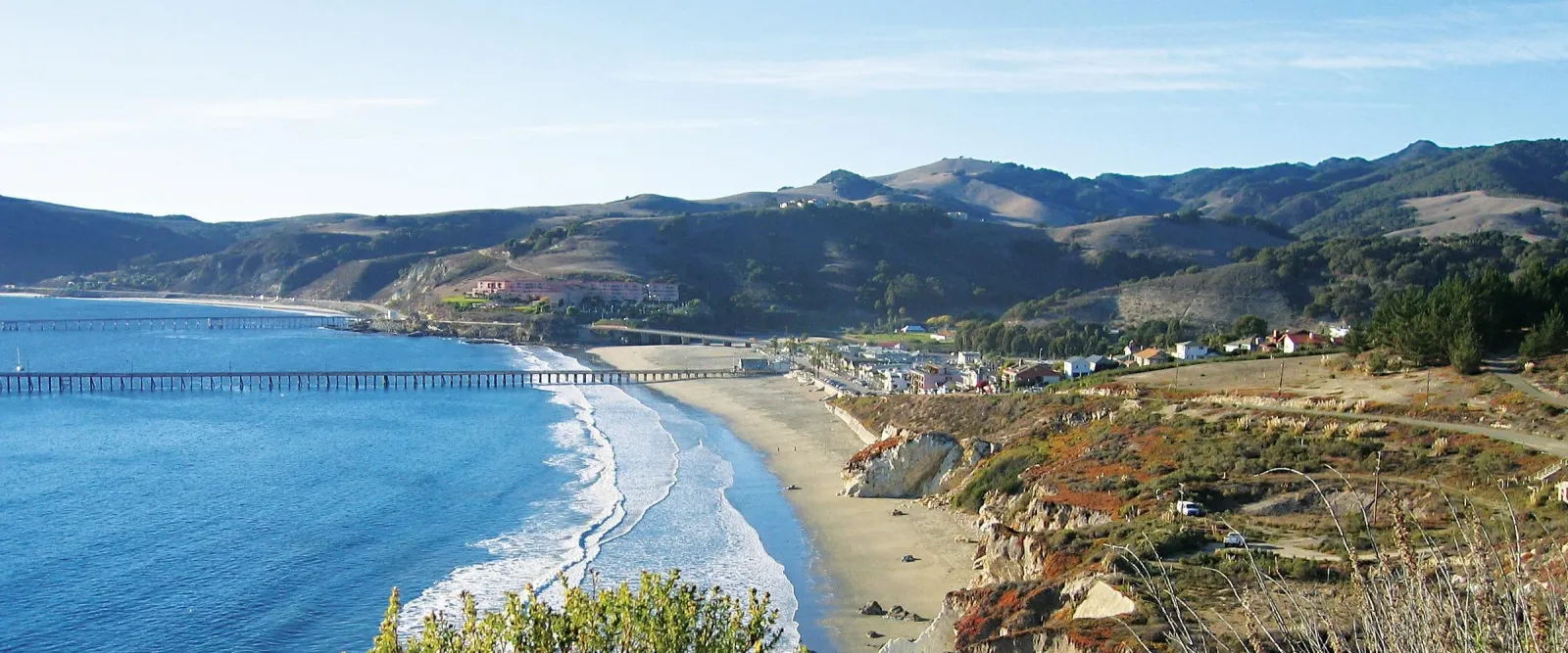 Scenic view of Avila Beach with piers and rolling hills in the background.