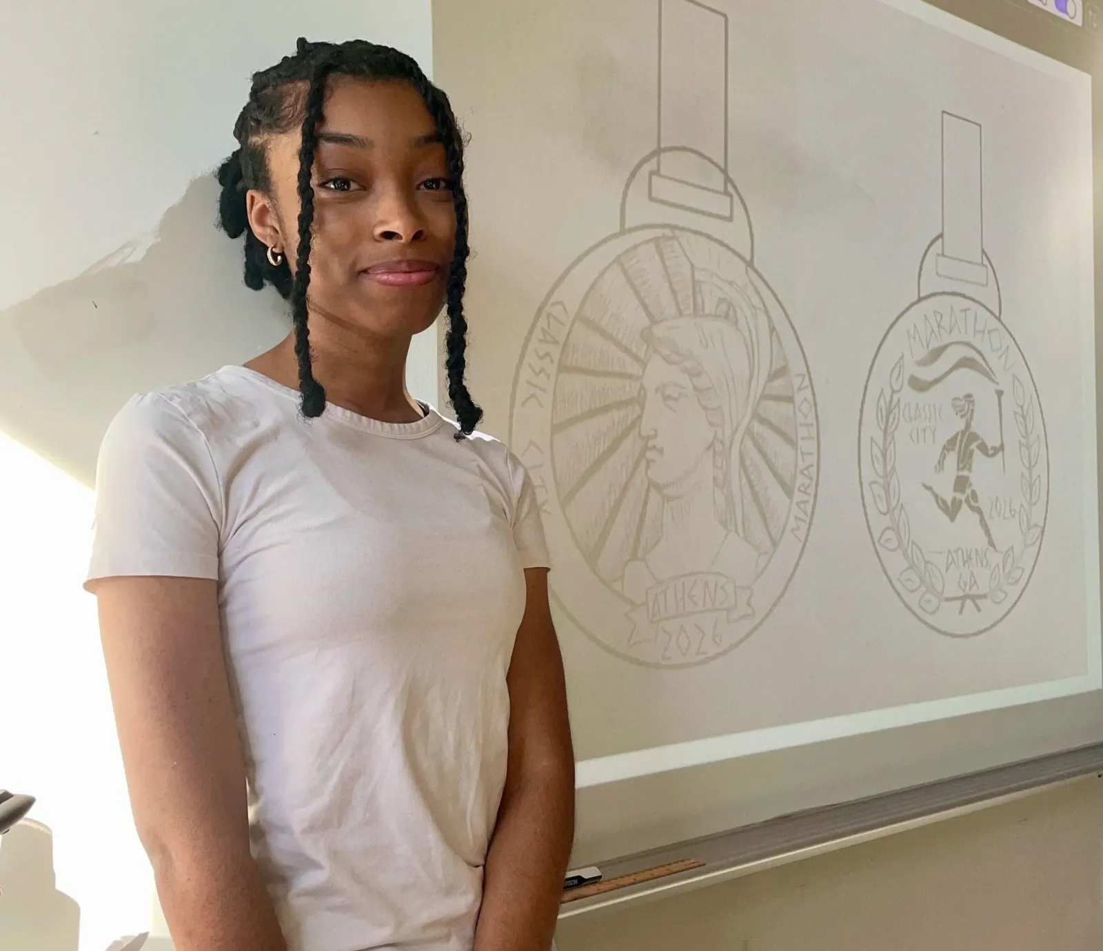 A young woman stands in front of a whiteboard displaying drawings of two race medals.