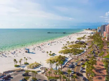 Aerial view of Clearwater Beach with the ocean, sand, palm trees, and buildings lining the street.
