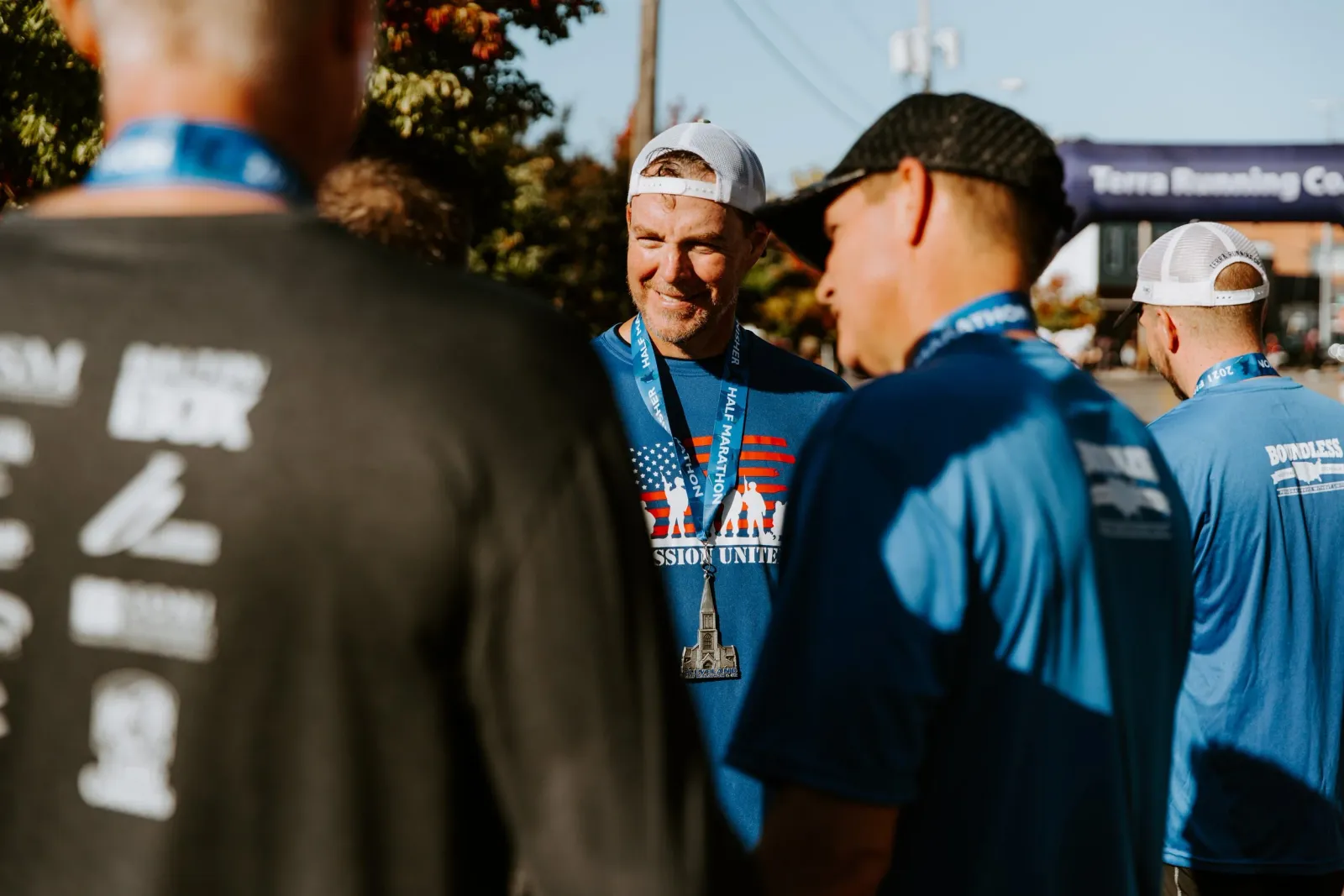 Runners wearing medals and race shirts chat near a finish line banner.