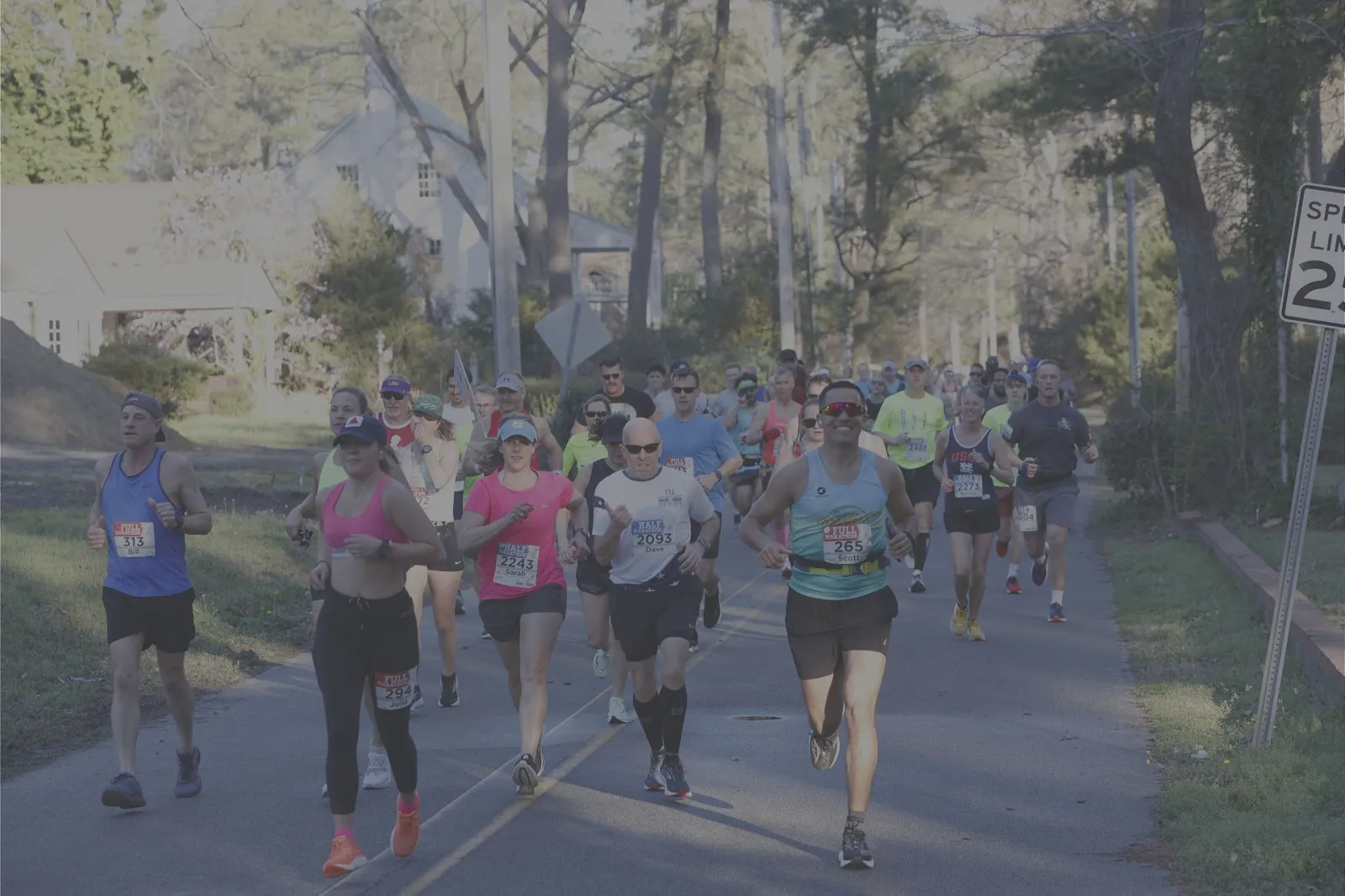 A group of runners participating in a road race, with some in the foreground and more in the background on a tree-lined street.