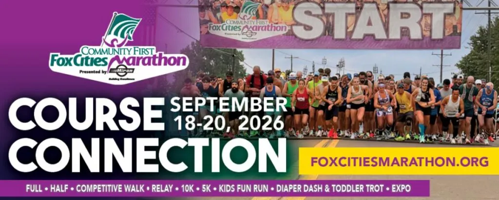 A large group of runners are lined up at the start of the Fox Cities Marathon, with a banner overhead that reads 'START'.