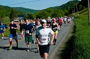 Runners on a road during the Covered Bridges Half Marathon, with rolling hills in the background.