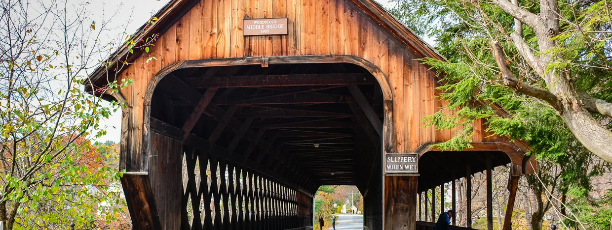 A wooden covered bridge with autumn foliage and a sign that reads 'Woodstock Middle Bridge 1969'.