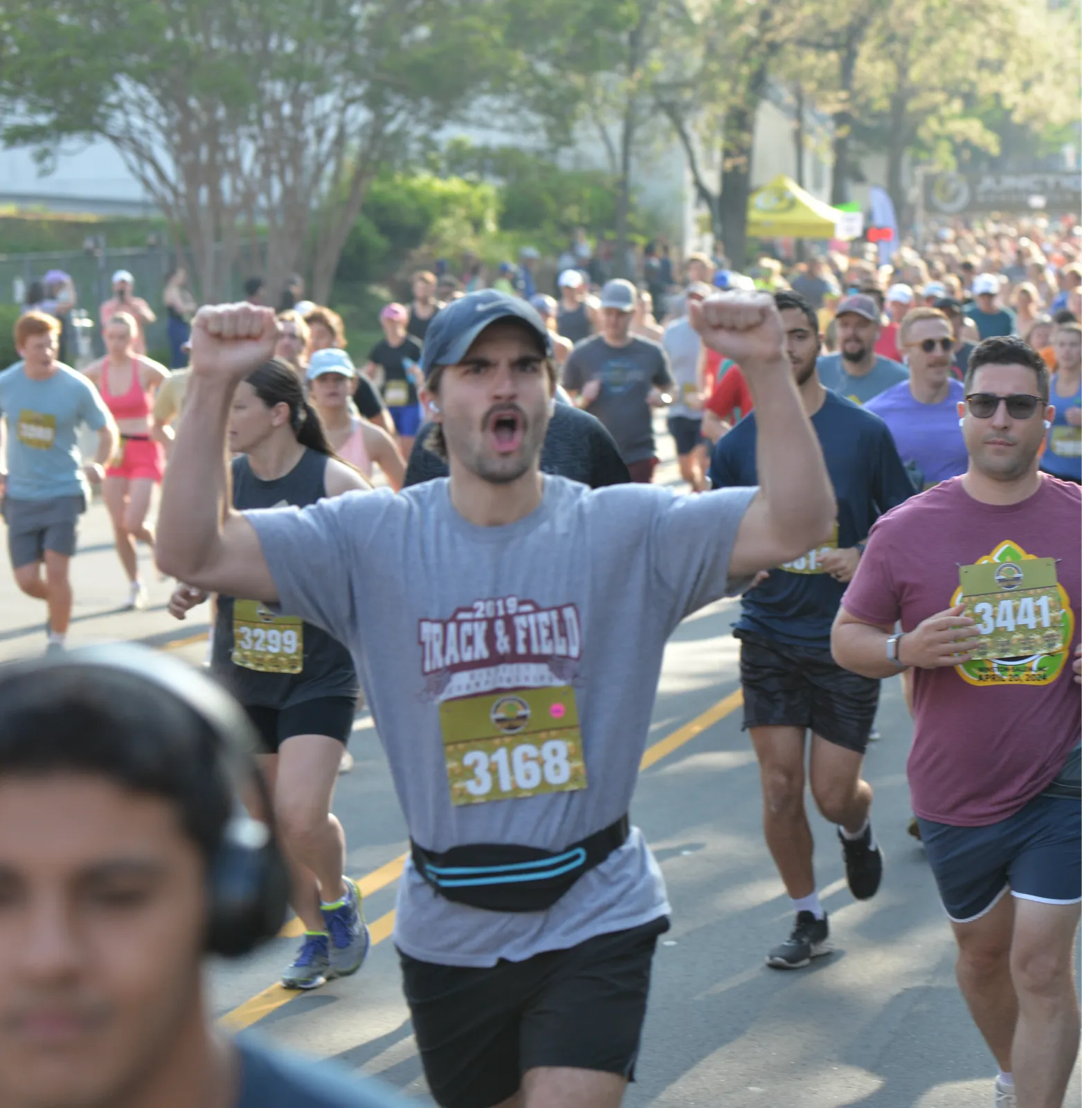 A runner with arms raised in excitement, surrounded by other participants during a race.