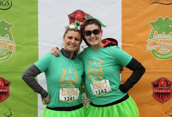 Two women in green St. Paddy's Day themed t-shirts and bright green tutus smile at the camera, with race bibs visible.