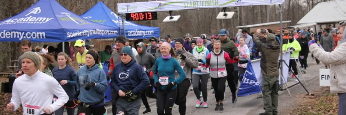 Runners at the start/finish line of a race, with tents and a digital clock in the background.