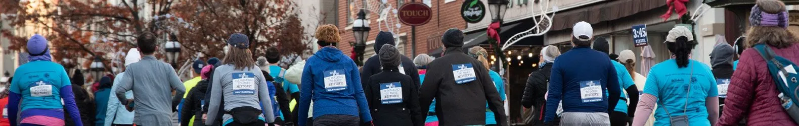 A group of runners participating in a half marathon, with many wearing blue shirts and bibs indicating they are walking to make history.