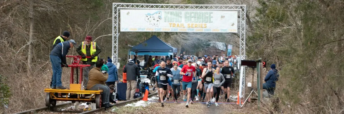 Runners at the start line of the King George Trail Series race, with a banner overhead.