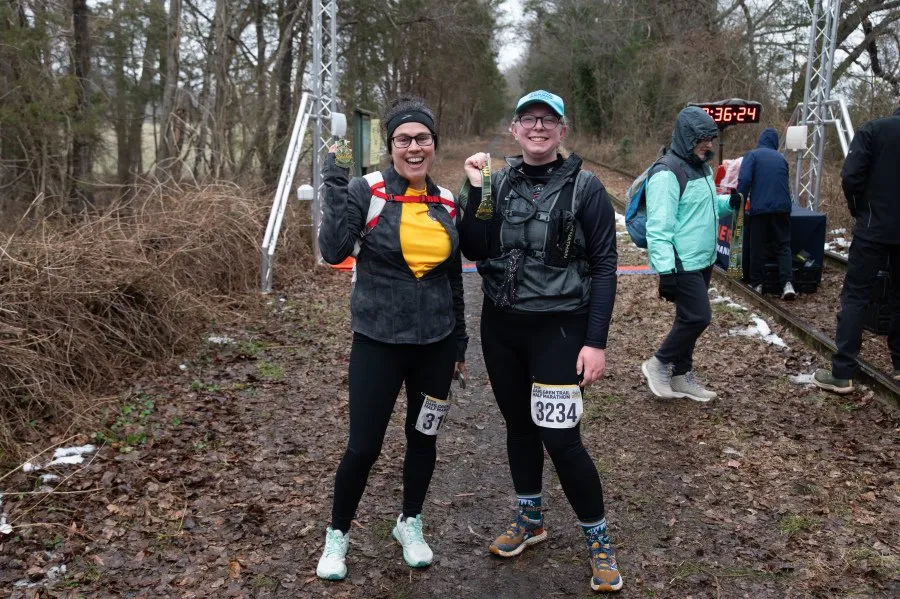 Two smiling runners proudly display their medals after completing the Dahlgren Trail Half Marathon.