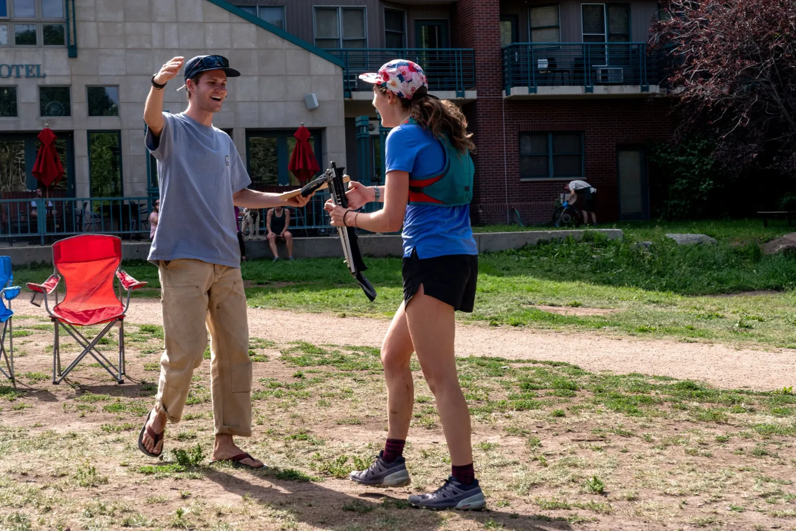 Two people, one in a blue shirt and the other in a grey shirt, interacting outdoors near a building, possibly at a race event.