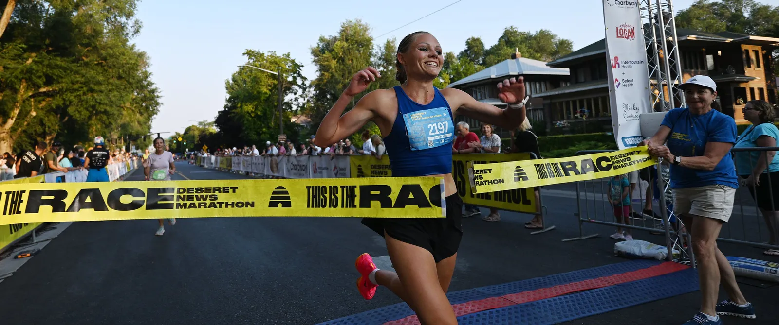 A female runner smiles as she breaks the finish line tape at the Deseret News Half Marathon.