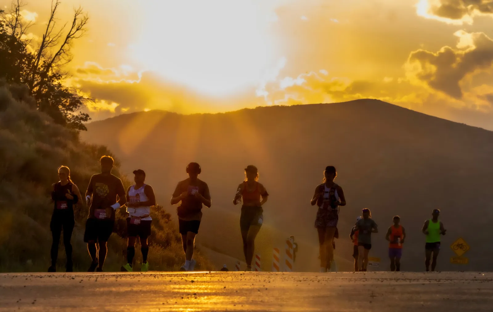 Runners on a road during a scenic sunrise or sunset, with mountains in the background.
