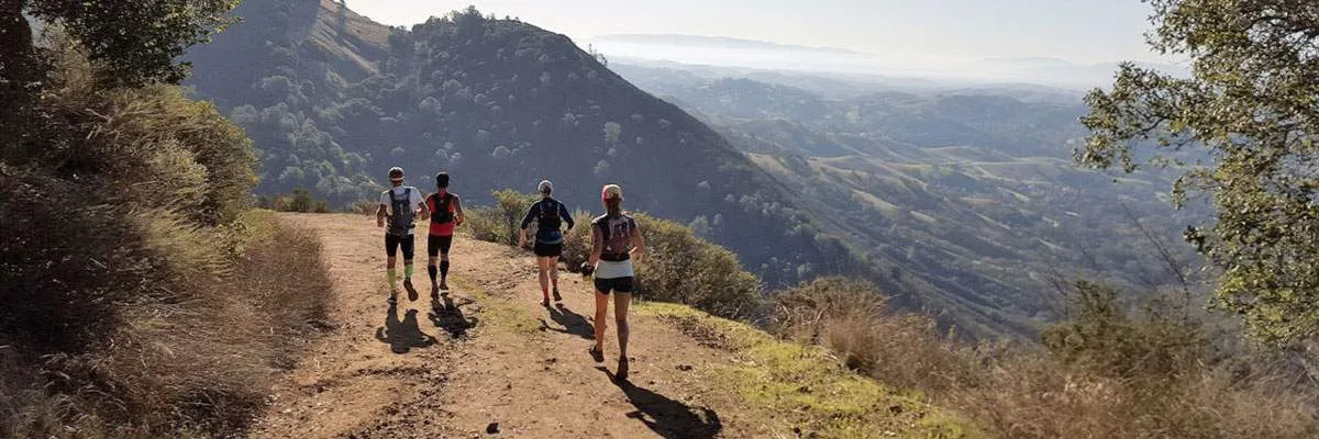 Runners on a dirt trail with rolling hills and mountains in the background.