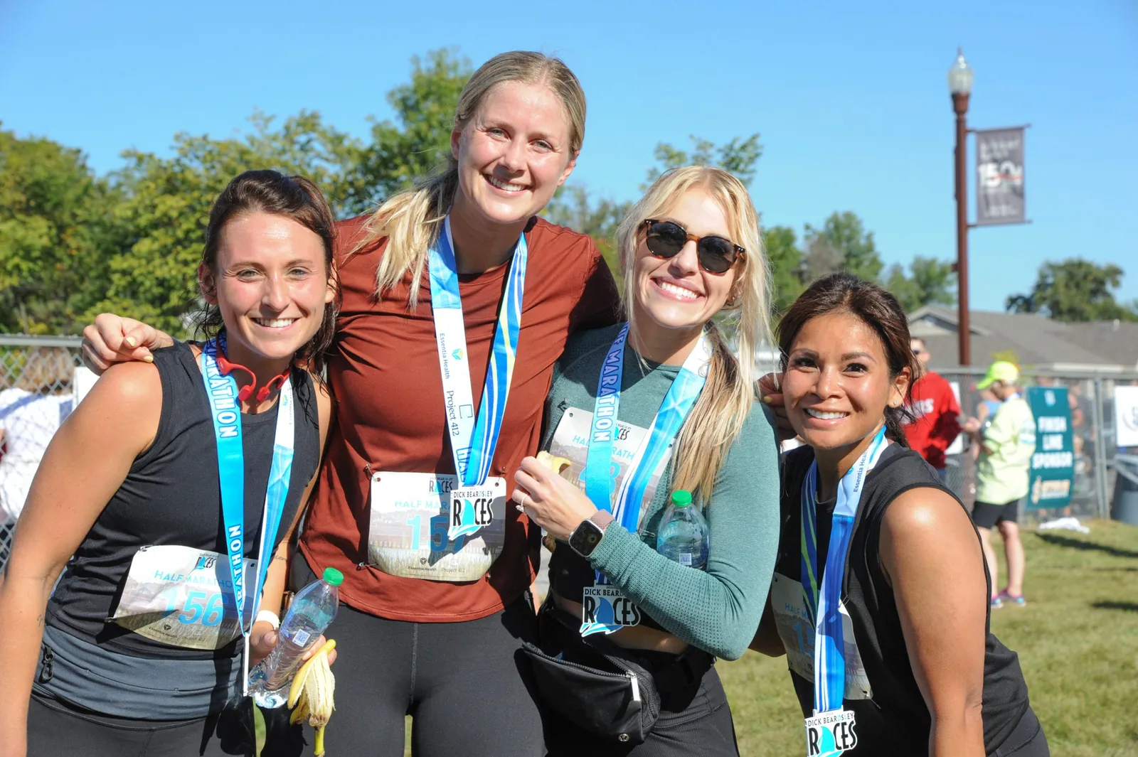 Four smiling women wearing race medals and bibs, posing for a photo after a half marathon.