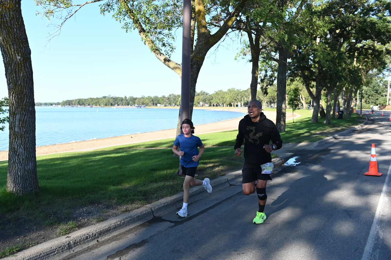 Two runners, one adult and one child, run along a paved path next to a lake.