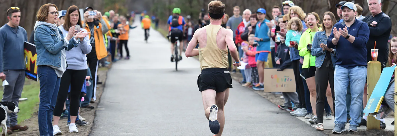 A runner is cheered on by a crowd of spectators lining a paved path.