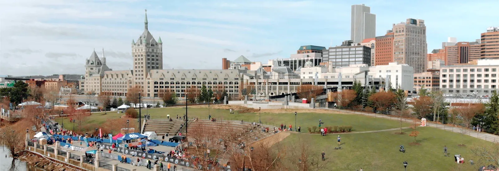 A panoramic view of a race start or finish area with tents and people, set against an urban skyline.