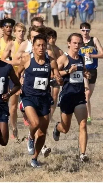 Runners in a race, with bib numbers visible, running on a dry, grassy course.