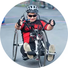 A wheelchair athlete in a black and red racing shirt and helmet competes in a road race.