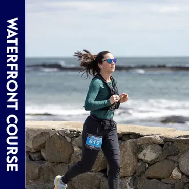 A female runner with bib number 619 runs along a waterfront course with the ocean in the background.