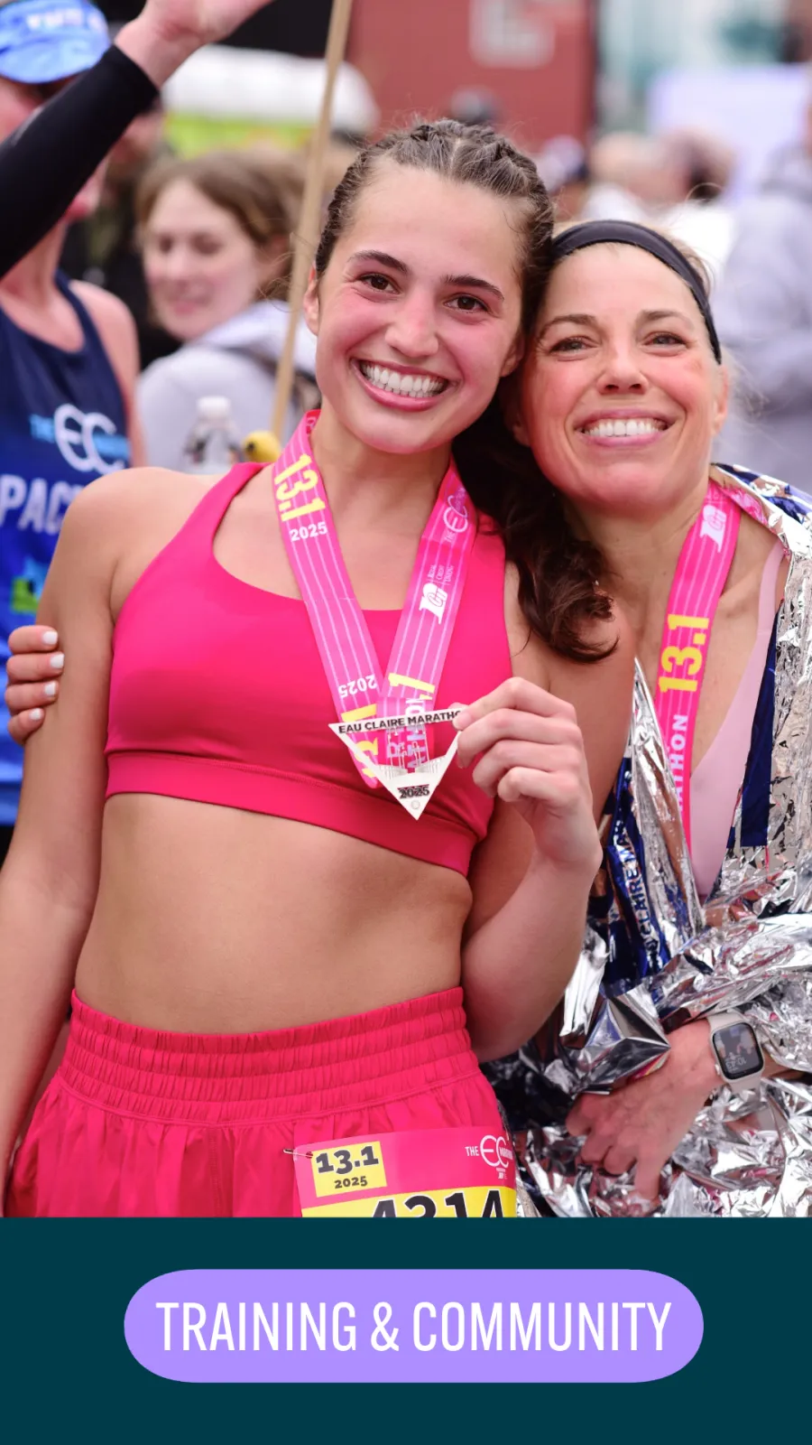 Two smiling female runners, one wrapped in a foil blanket, pose for a photo after a race, both wearing medals.