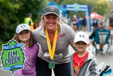 A woman and two children smile at the camera, wearing race medals and with a finish line in the background.