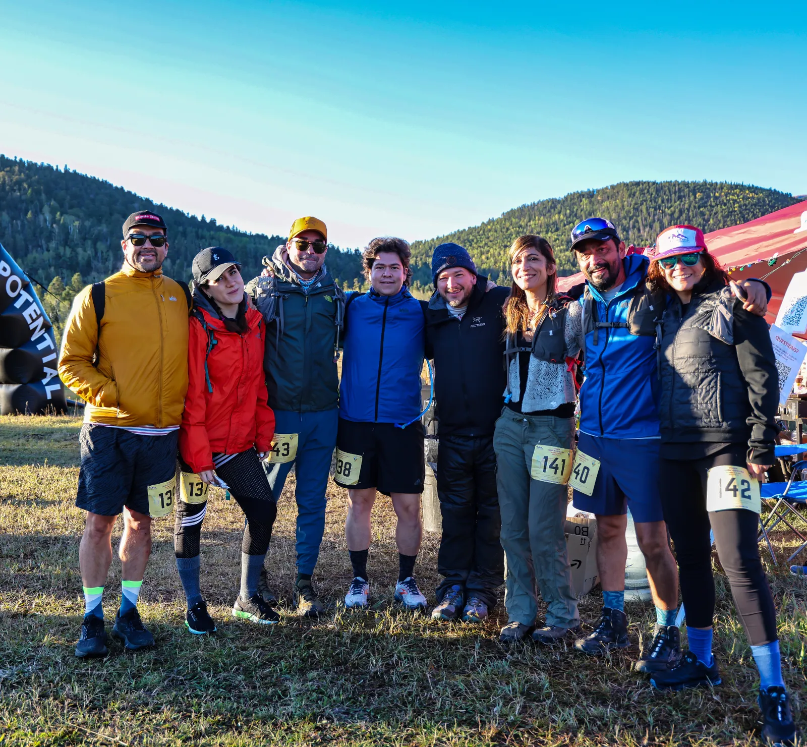 A group of eight runners pose for a photo before a trail race, with mountains in the background.