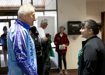 Two people talking at a race event, with other participants in the background.