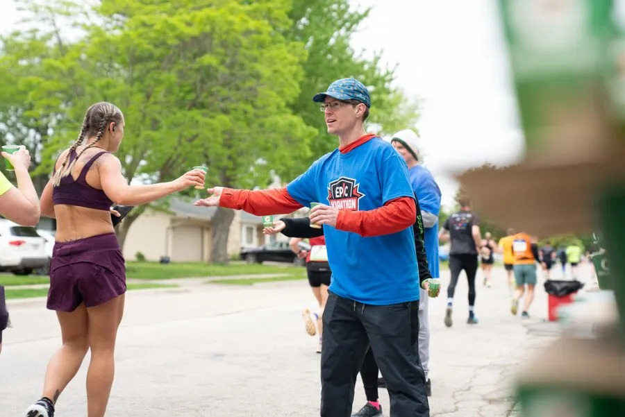 A female runner receives a cup from a male volunteer at a water station during a race.