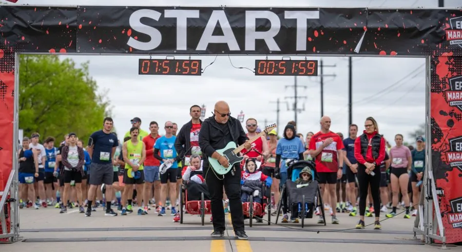 A crowd of runners gathered at the start line of a race, with a man playing a guitar in the foreground.