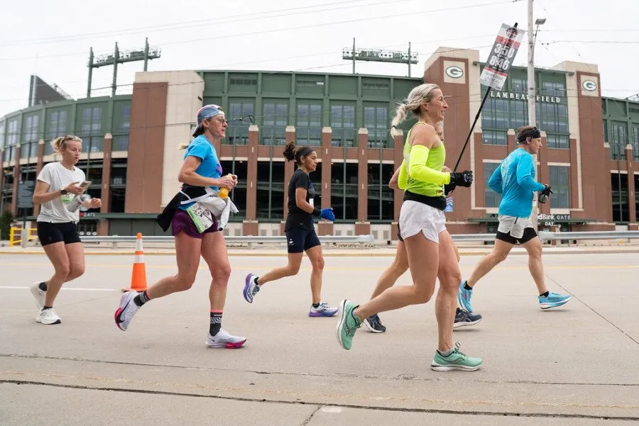 Runners on a road course with Lambeau Field in the background.
