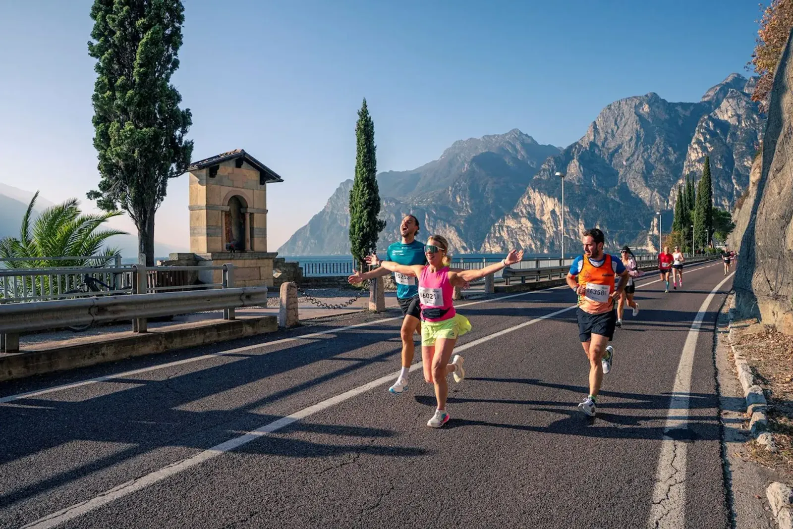 Runners celebrating as they race along a scenic road next to a body of water with mountains in the background.