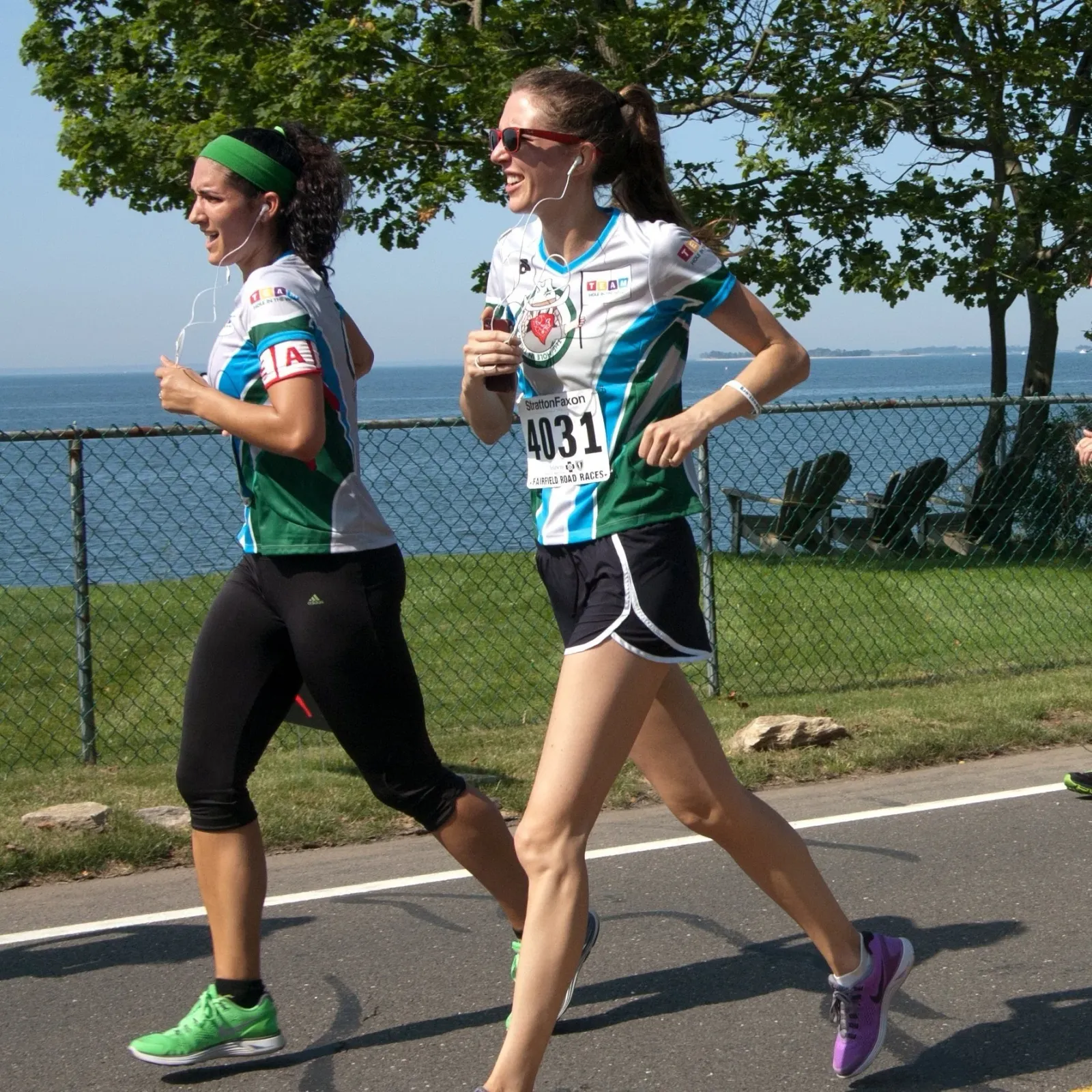 Two female runners on a road course with a waterfront view.