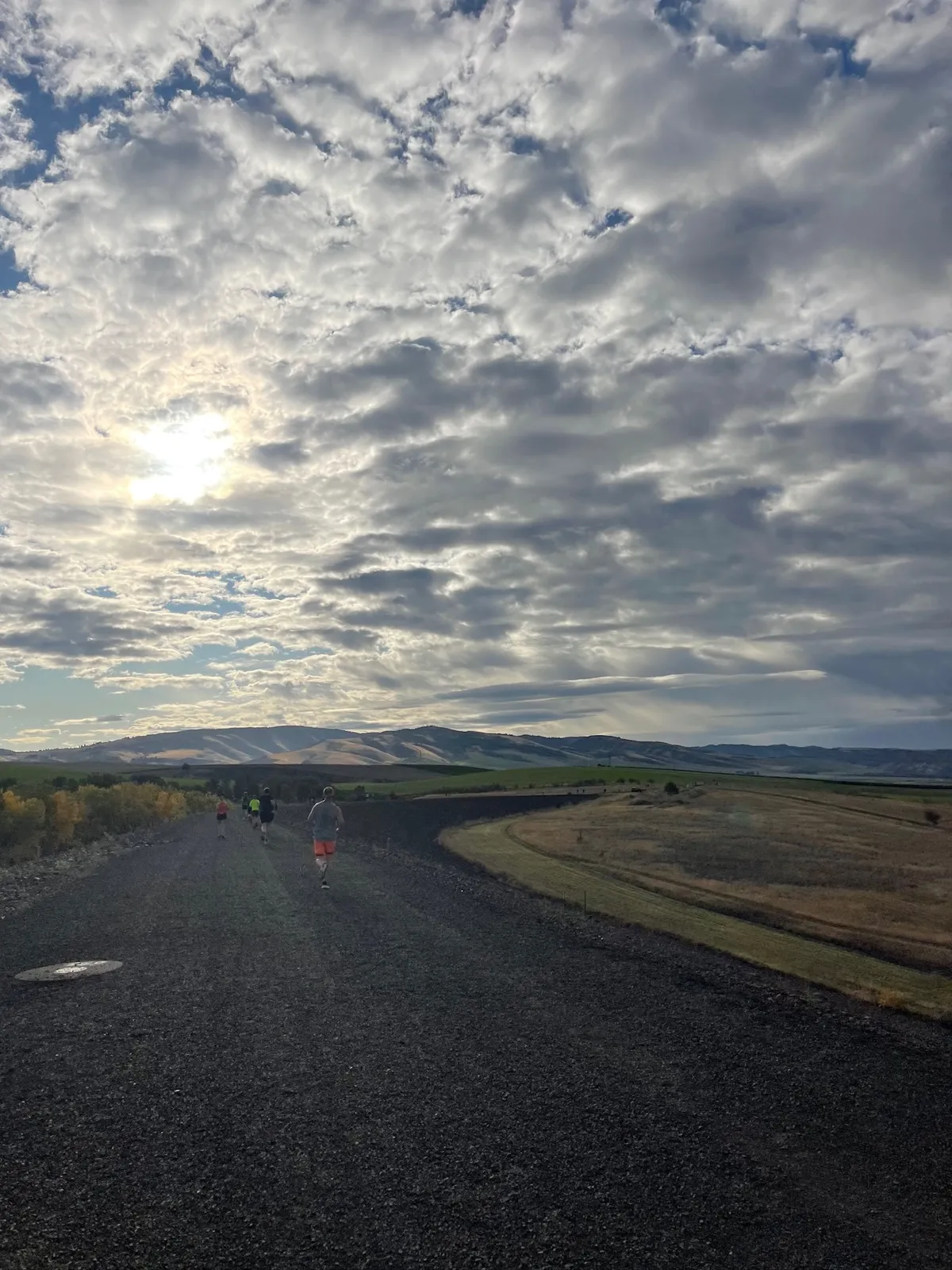 Runners on a gravel path with rolling hills and a cloudy sky in the background.