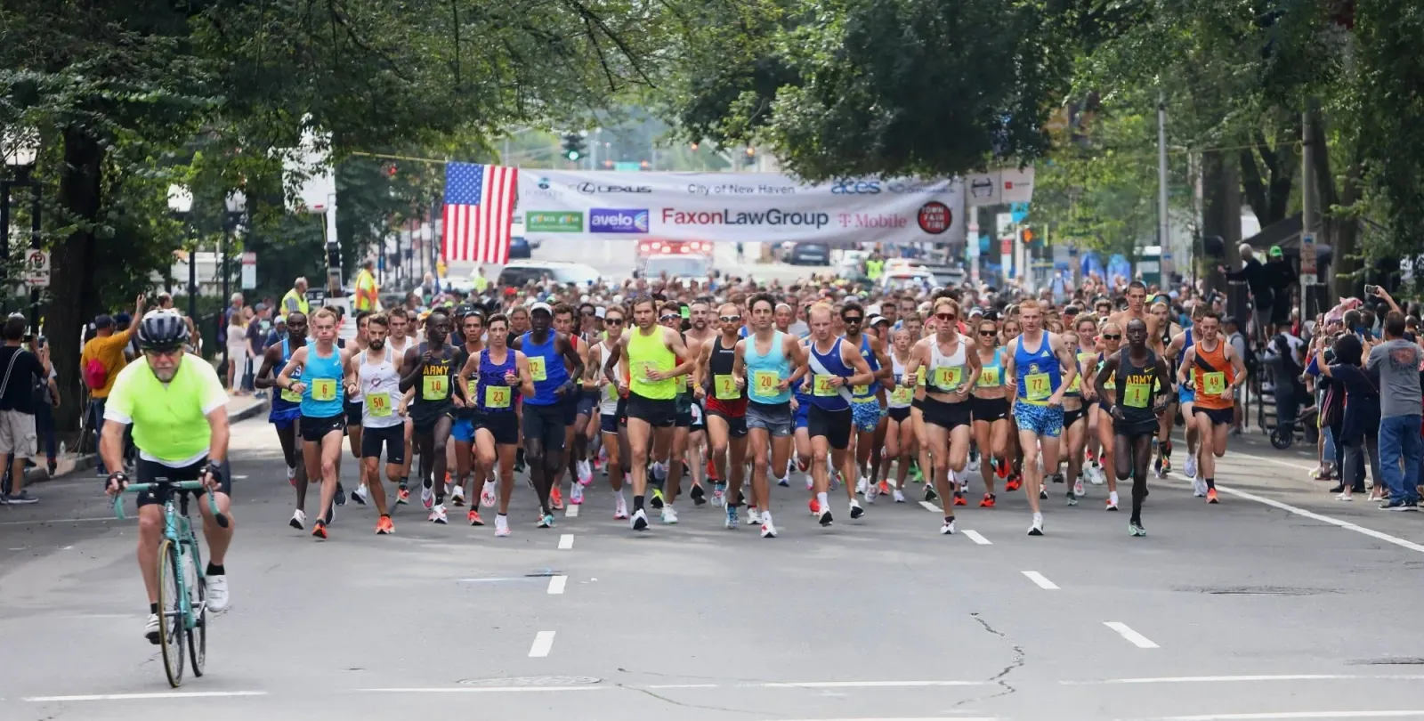 Runners starting a road race with a banner overhead and spectators on the side.