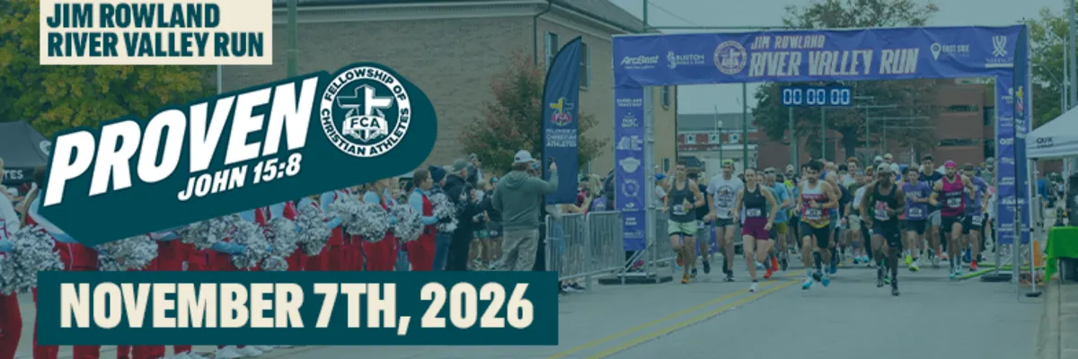Runners starting the Jim Rowland River Valley Run on November 7th, 2026, with a large banner overhead and cheerleaders on the side.