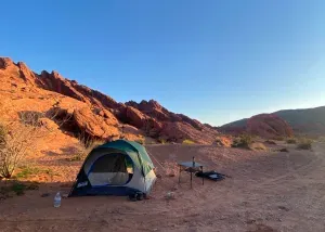 A tent set up in a desert landscape with red rock formations under a clear blue sky.