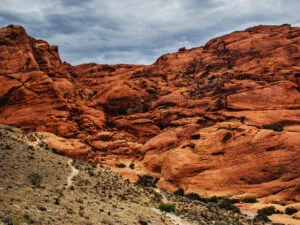 Red rock formations with a trail winding through the landscape under a cloudy sky.