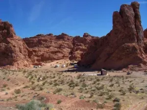 Scenic desert landscape with red rock formations and scattered camping tents under a clear blue sky.