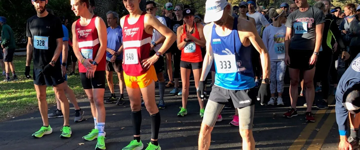 Runners in athletic wear and bib numbers gathered at the start line of a road race.