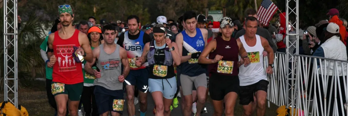 A diverse group of runners are lined up at the start of a race, with some looking ahead with determination and others smiling.
