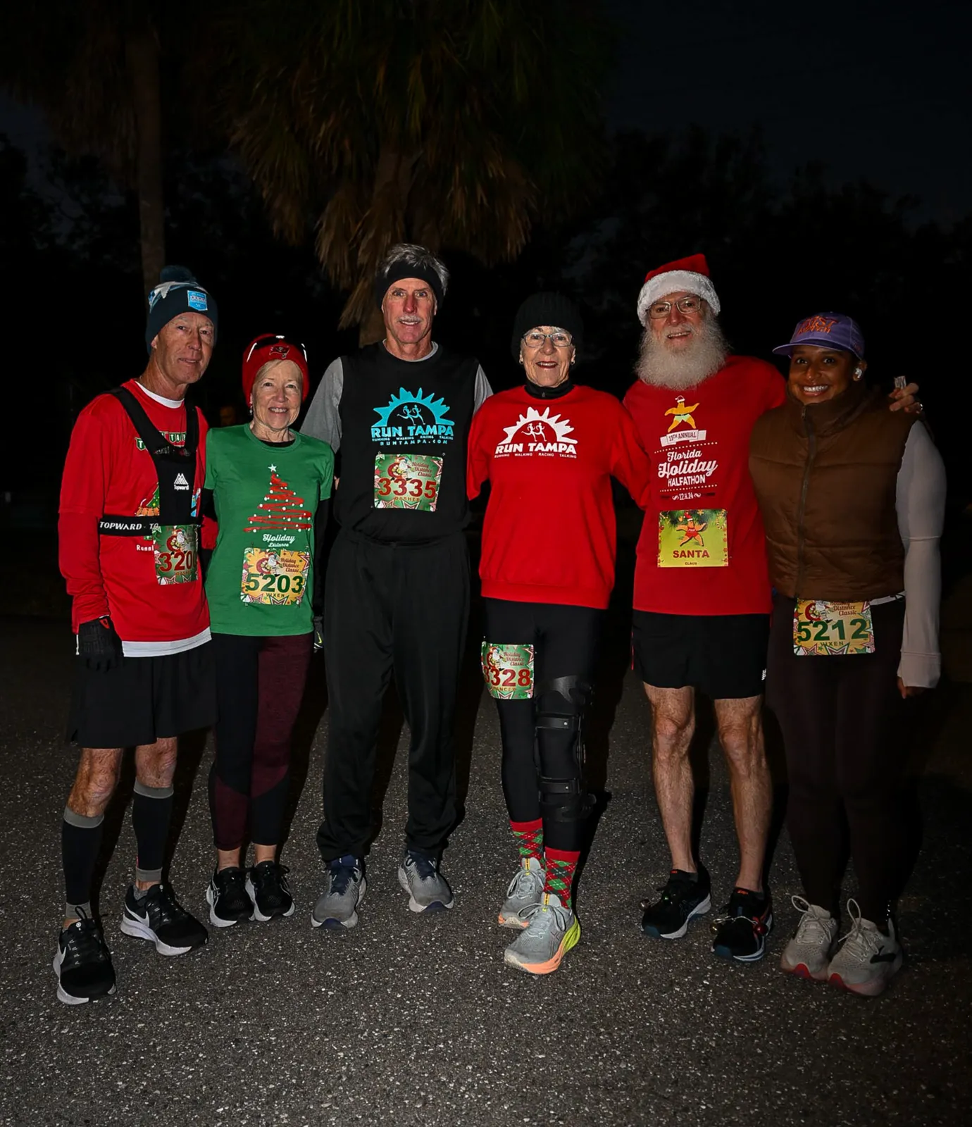 A group of six runners, including one dressed as Santa, pose for a photo before or after a holiday race.