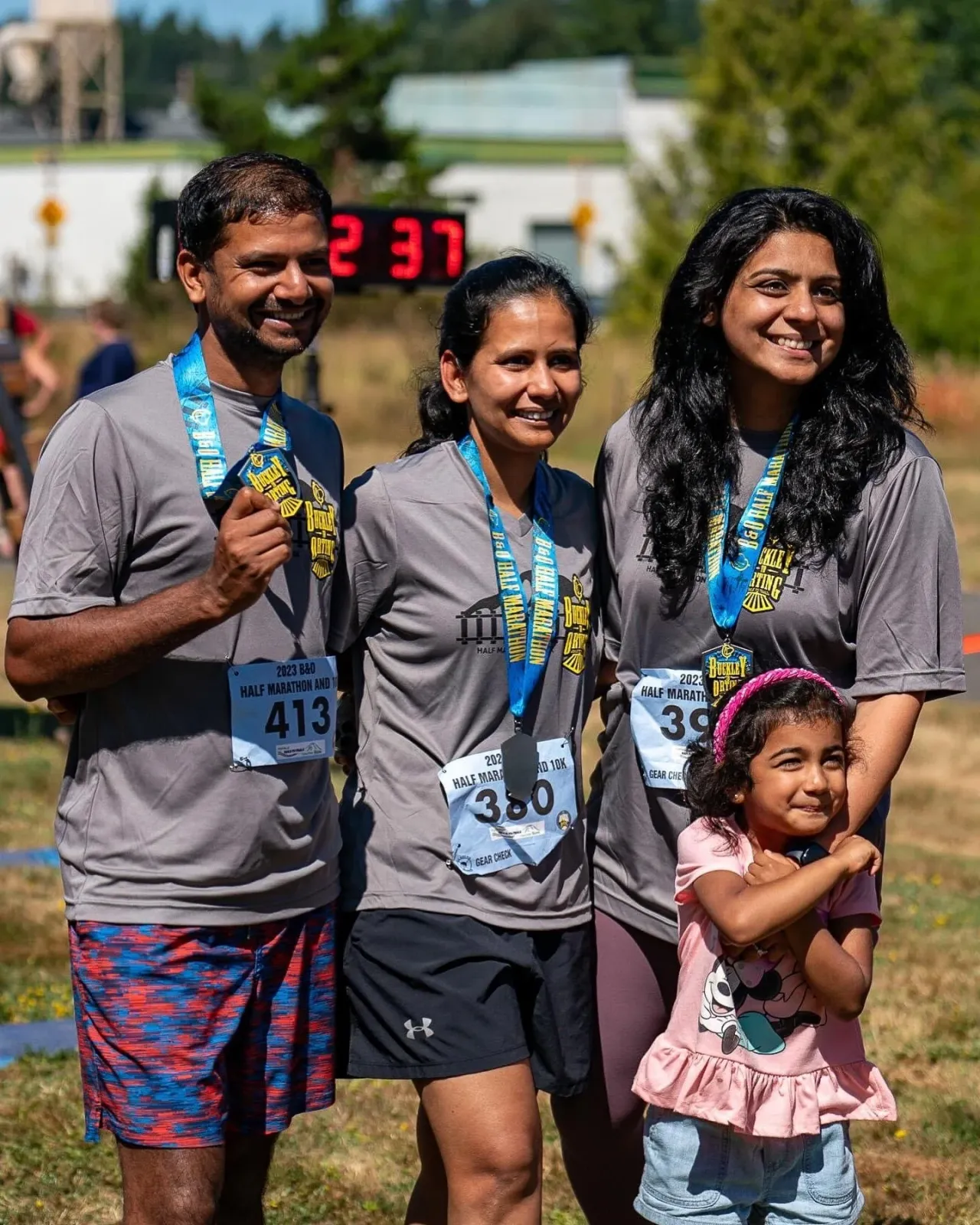 A group of three adults and a young child smiling, all wearing race medals and bibs, suggesting a successful completion of a half marathon.
